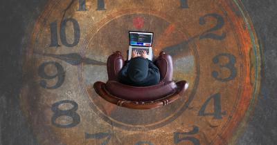 Laptop user with a clock in background
