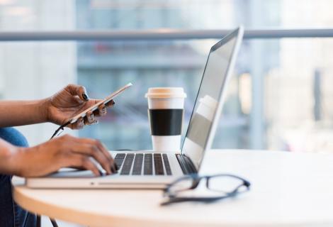Woman working on a laptop and using her mobile phone to confirm her identity