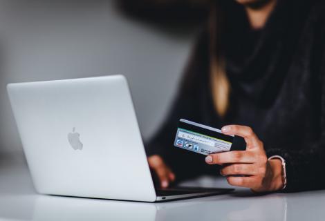 Person holding a credit card as they sit as a laptop